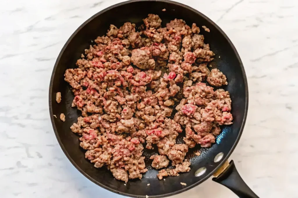 A skillet of ground beef being cooked and browned, ready for layering in the casserole.