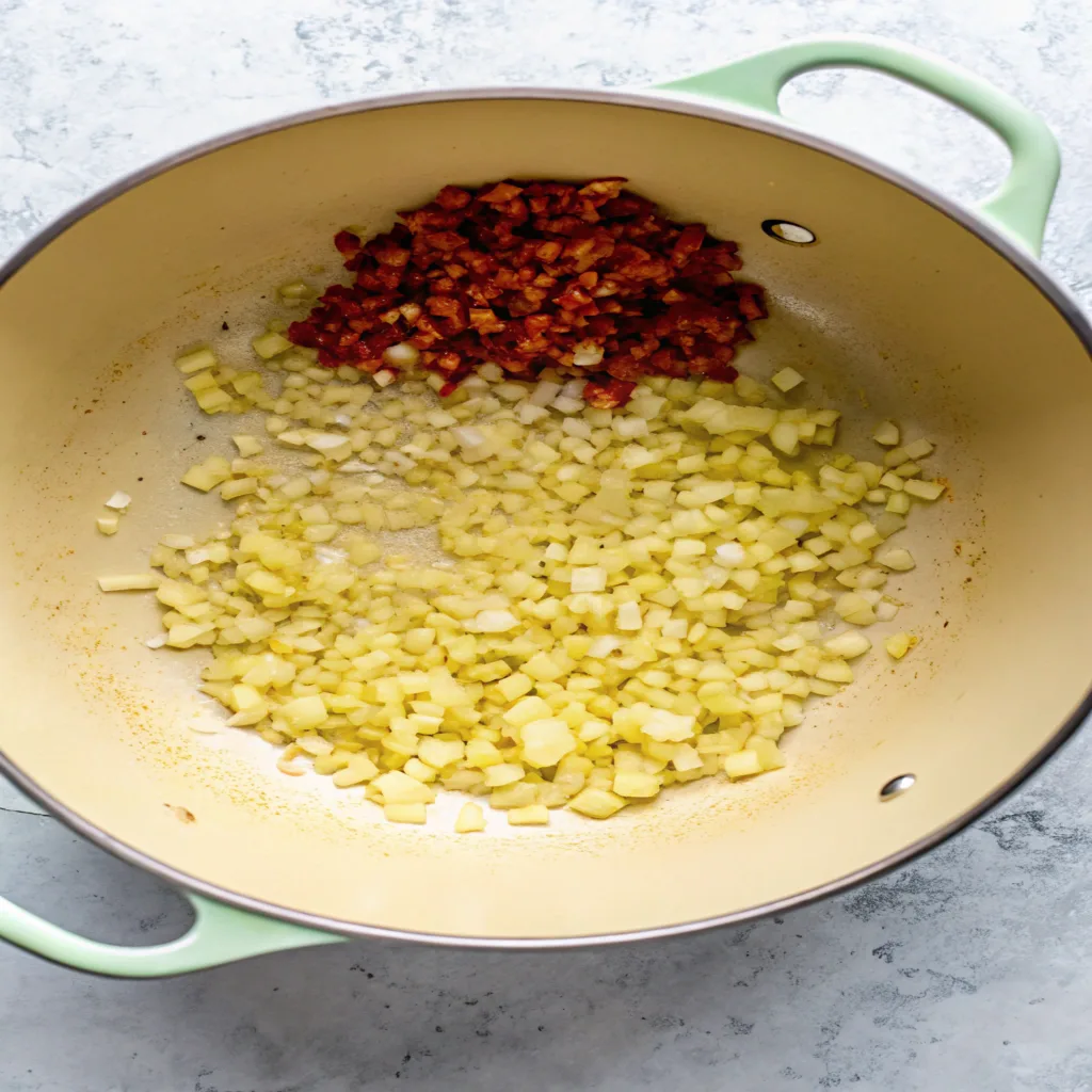 A pot showing diced onions and chorizo being sautéed together, forming the flavorful base for Marry Me Chicken Soup.