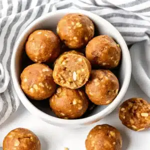Bowl filled with no-bake peanut butter protein energy bites, some with visible chopped nuts and seeds
