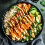 Overhead view of a crispy chicken rice bowl topped with spicy mayo, cucumbers, and green onions