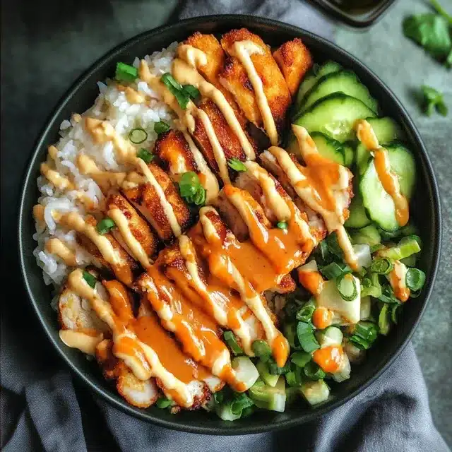 Overhead view of a crispy chicken rice bowl topped with spicy mayo, cucumbers, and green onions
