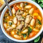 A bowl of hearty Italian sausage and white bean soup with carrots, onions, greens, and a savory broth.