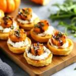 Mini puff pastry tarts topped with creamy goat cheese, roasted butternut squash rounds, fresh herbs, and a balsamic glaze on a wooden board.