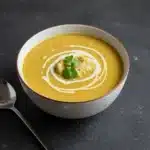 Bowl of creamy golden soup topped with cream swirls, breadcrumbs, and fresh cilantro garnish