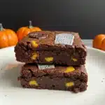 Close-up of fudgy chocolate brownies with yellow candy pieces, decorated with edible tombstone toppers and pumpkins in the background.