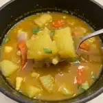 Bowl of Ecuadorian-style vegetable soup with chunks of yellow squash, red bell pepper, corn, and herbs in a golden broth.