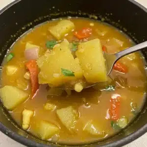 Bowl of Ecuadorian-style vegetable soup with chunks of yellow squash, red bell pepper, corn, and herbs in a golden broth.