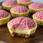 Halloween-themed mini cheesecake cupcake with pink brain frosting, graham cracker crust, and a bite taken out.