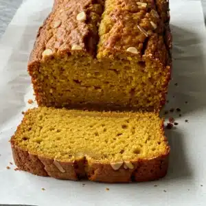 A sliced loaf of golden-brown homemade pumpkin bread topped with slivered almonds, resting on parchment paper.