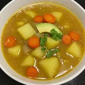Bowl of potato and carrot soup with onion, avocado slice, and fresh cilantro in a golden broth