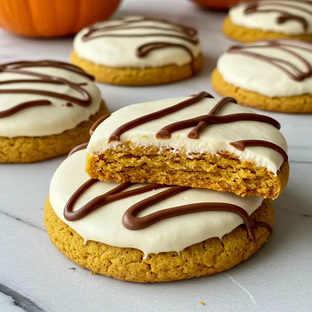 Frosted pumpkin cookies topped with cream cheese icing and chocolate drizzle, with one cookie showing a moist interior.