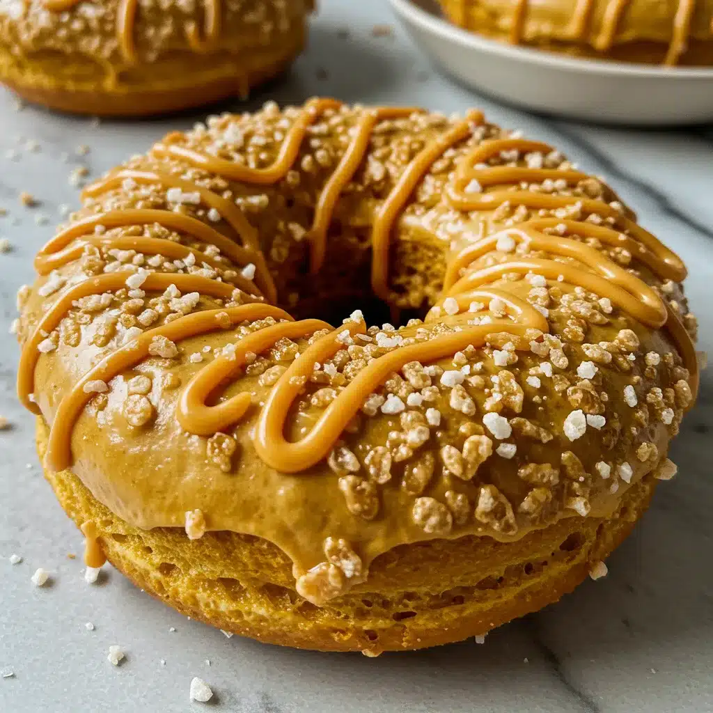 Close-up of a pumpkin spice donut topped with caramel drizzle and crunchy sugar crystals on a marble surface.