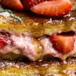 Strawberry cheesecake stuffed French toast topped with fresh strawberries and syrup.